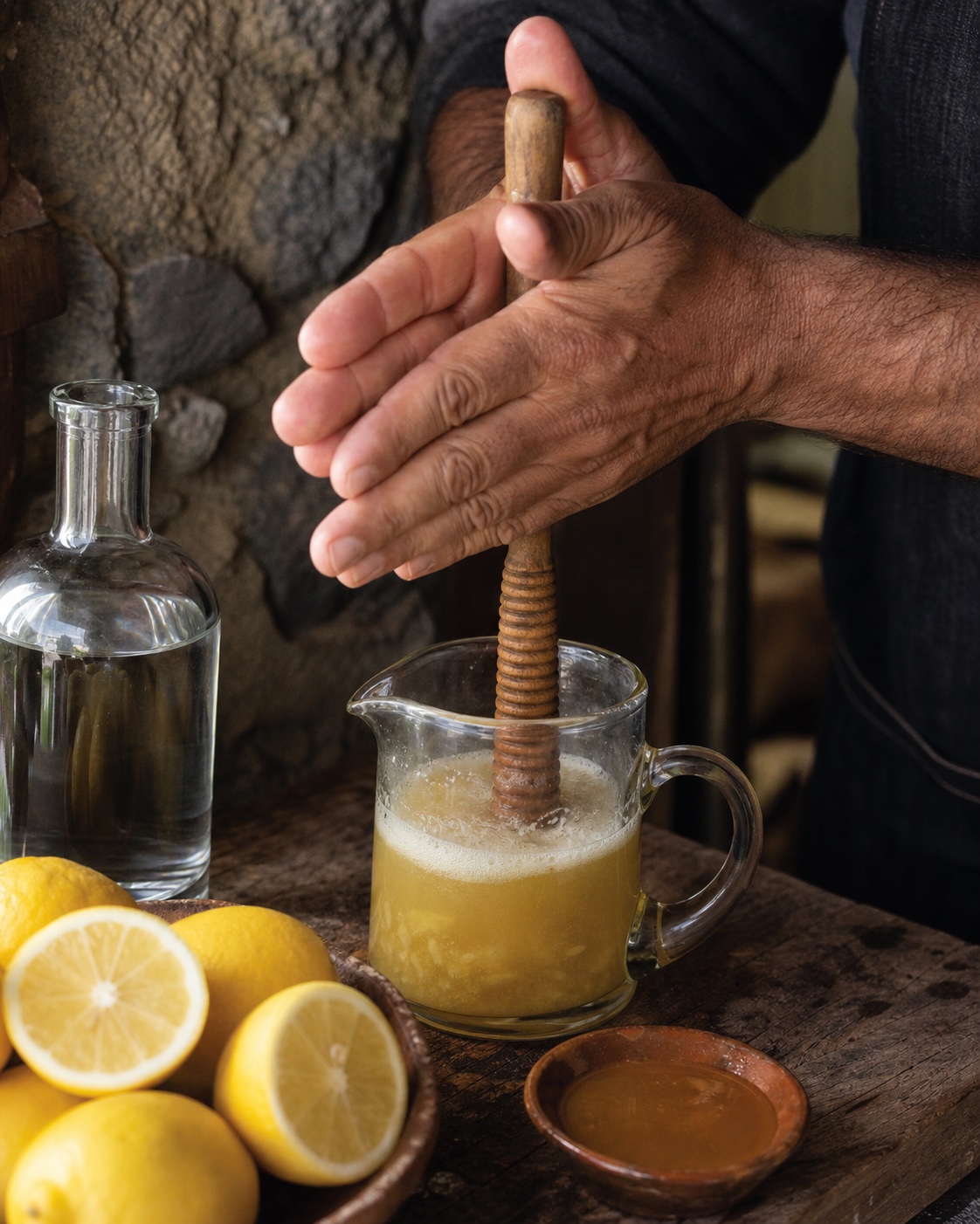 Mãos a misturar poncha fresca com um mexelote tradicional de madeira